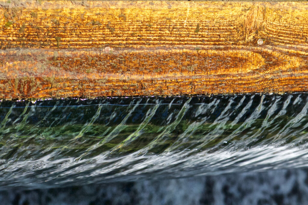Wasser fließt über ein Holzschott aus einem Teich ab