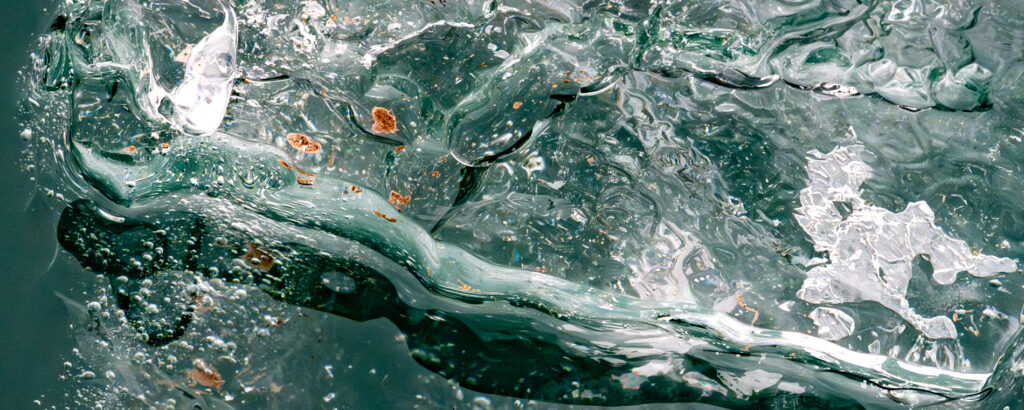 Wasser und Eis, Lufteinschlüsse, eingefrorenes organisches Material, schwimmend im petrolfarbenen arktischen Meer um Spitzbergen